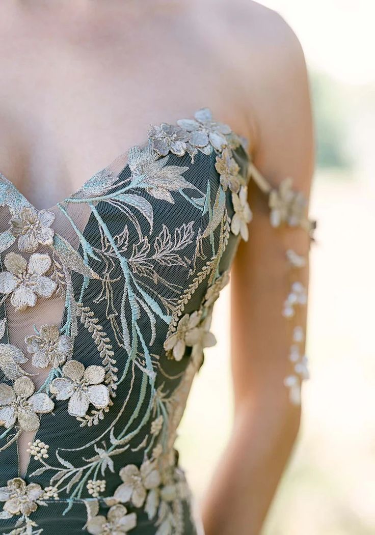 a woman wearing a dress with flowers on the back and shoulder, standing in a field