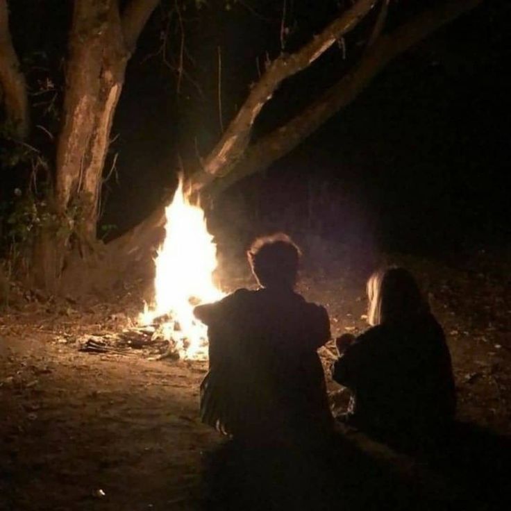 two people sitting around a campfire at night