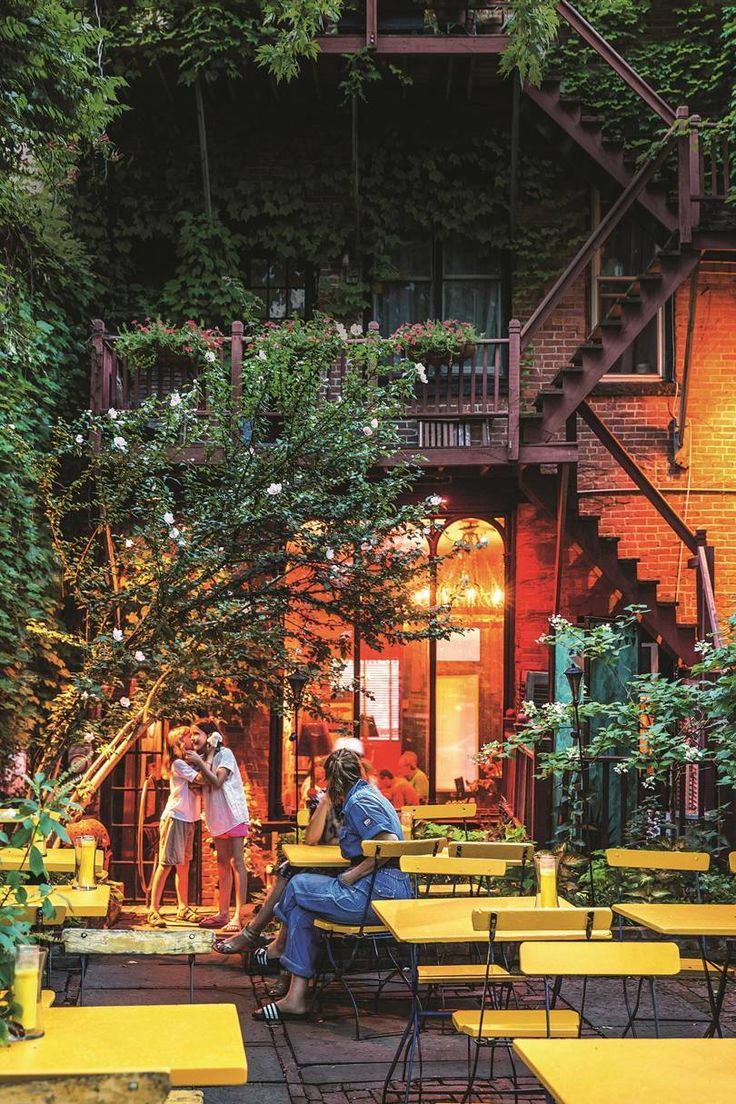 people sitting at yellow tables in front of a building with ivy growing on the walls