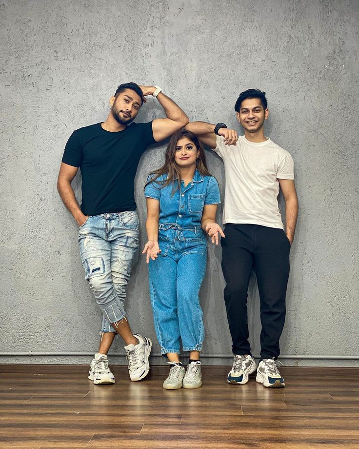 three people standing next to each other in front of a wall and wood flooring