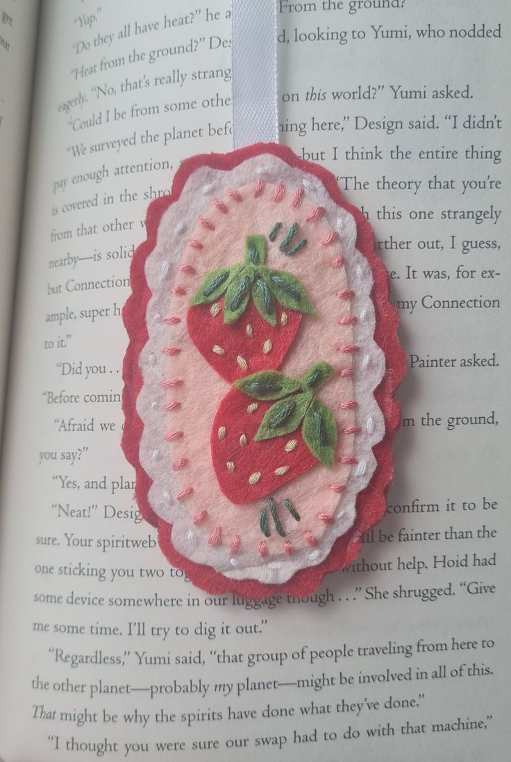 the book is open to show an embroidered brooch with two strawberries on it