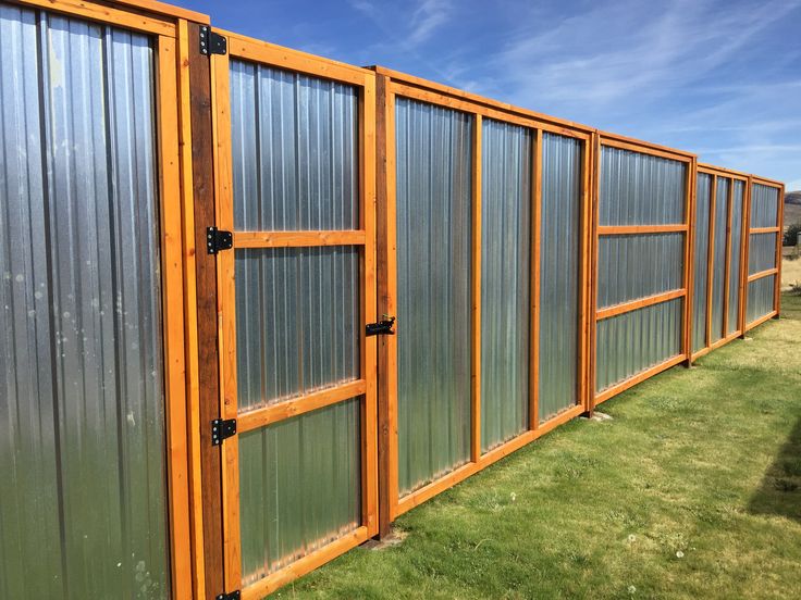 a large metal fence with wooden posts and windows on it's sides in the grass