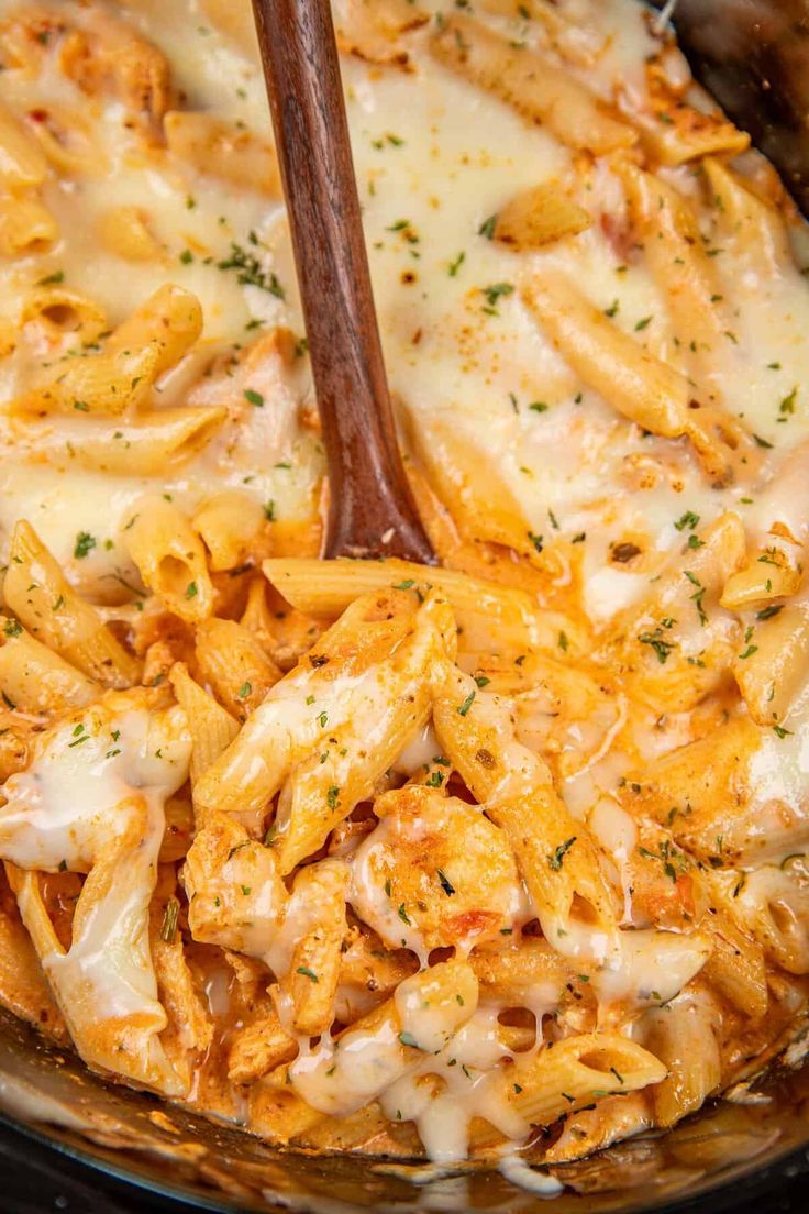 a wooden spoon is stirring pasta in a skillet with cheese and parmesan