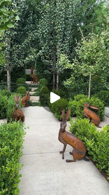 an outdoor garden with metal rabbits in the center and bushes around it on either side