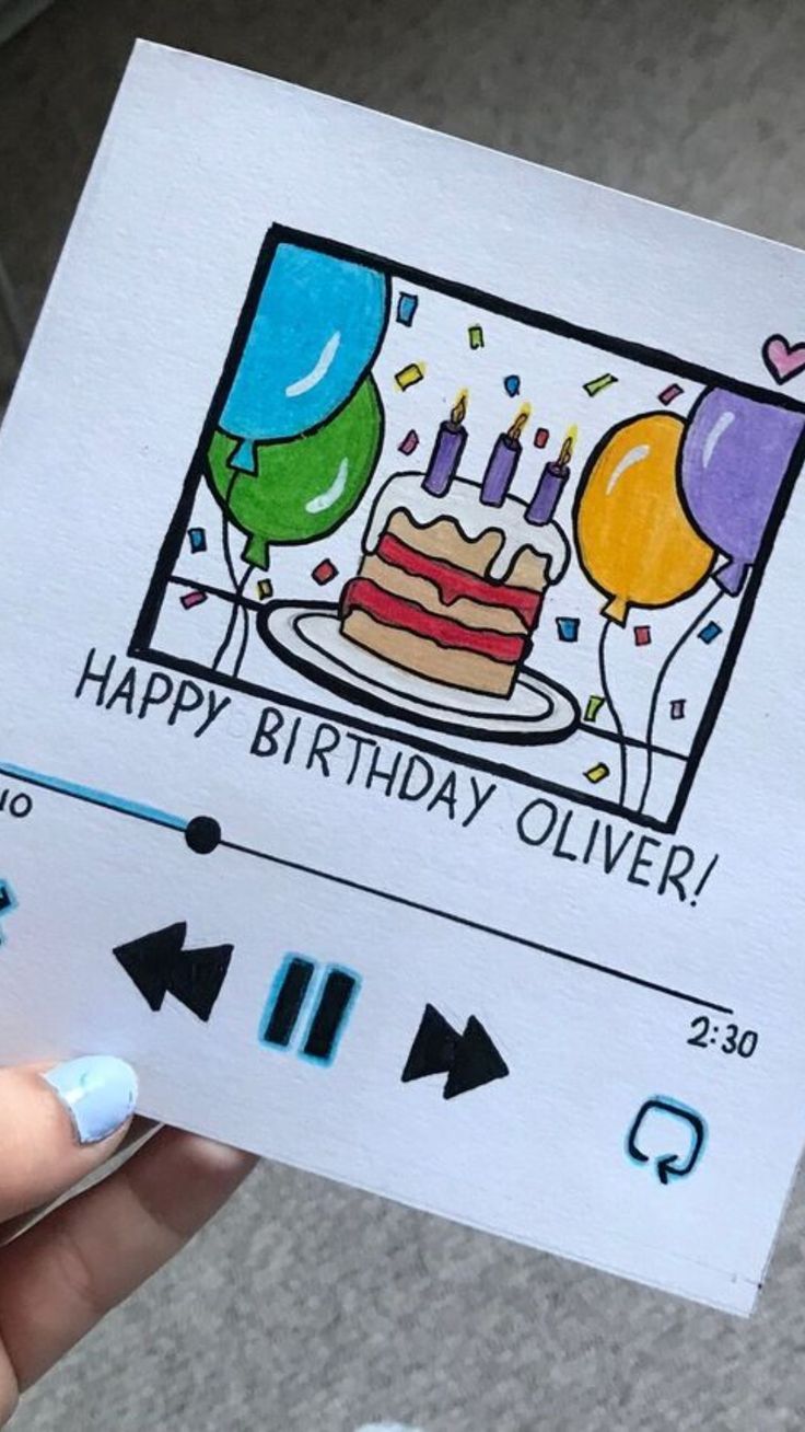 a person holding up a birthday card with balloons and a cake in the box on it