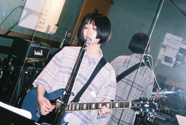 a young man holding a guitar while standing in front of a microphone and another person behind him