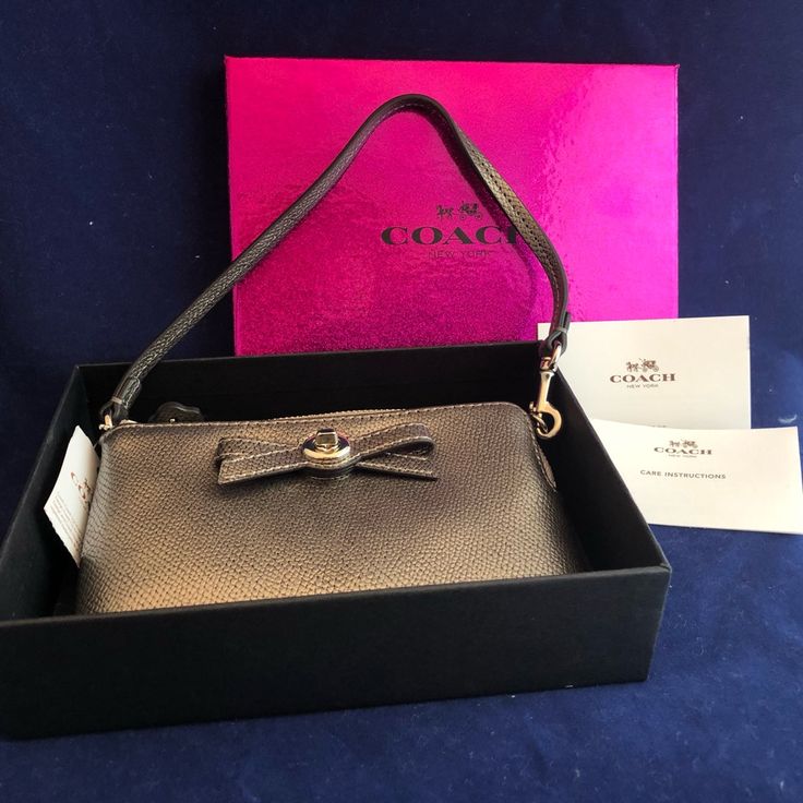 a gold purse with a bow on the front in a black box next to a pink card