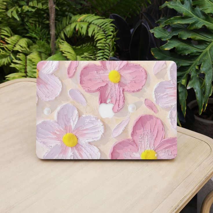 a pink and white flowered laptop sitting on top of a wooden table next to green plants