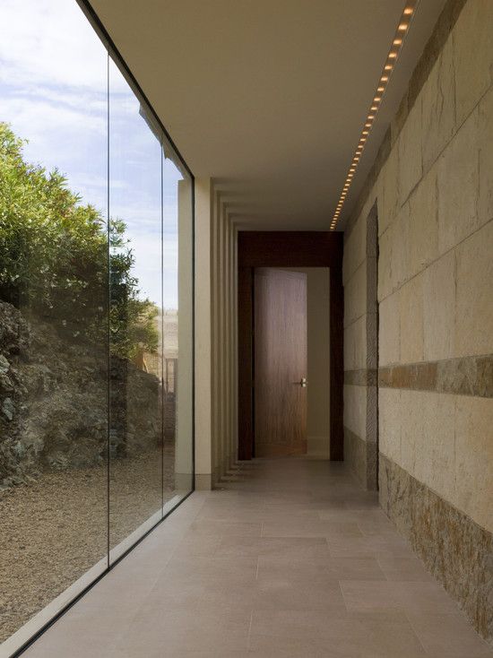 an empty hallway with glass walls leading to the outside area and trees in the background