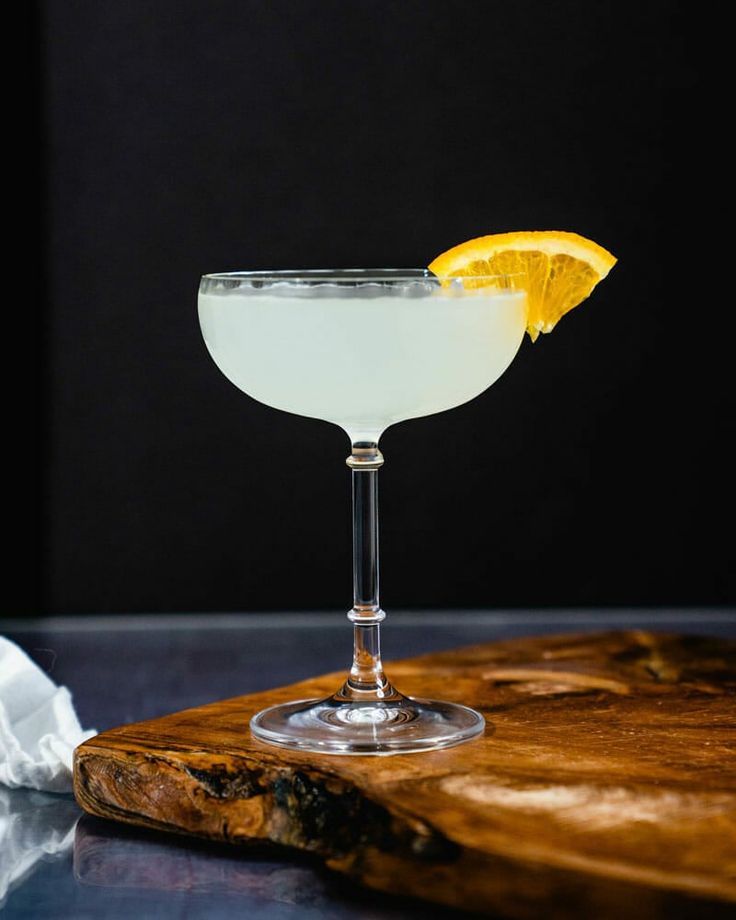 a glass filled with white liquid sitting on top of a wooden cutting board next to a slice of lemon