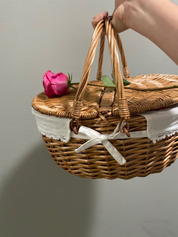 a woman's hand holding a wicker basket with a pink rose on it