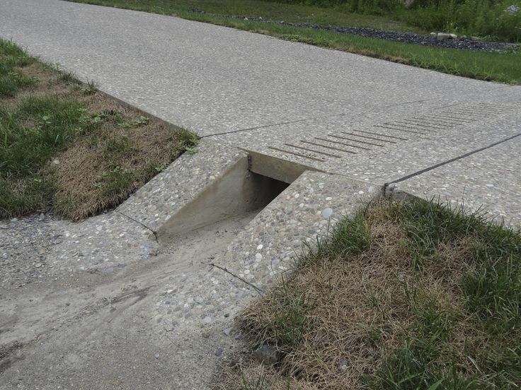 an open hole in the ground with grass and rocks around it on a paved road