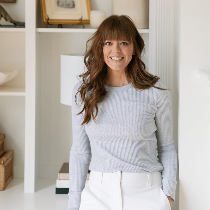 a woman standing in front of a white book shelf with books on top of it