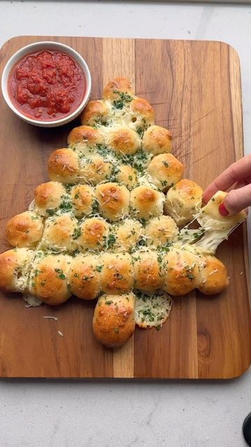 a christmas tree made out of rolls on a cutting board with dipping sauce in the background