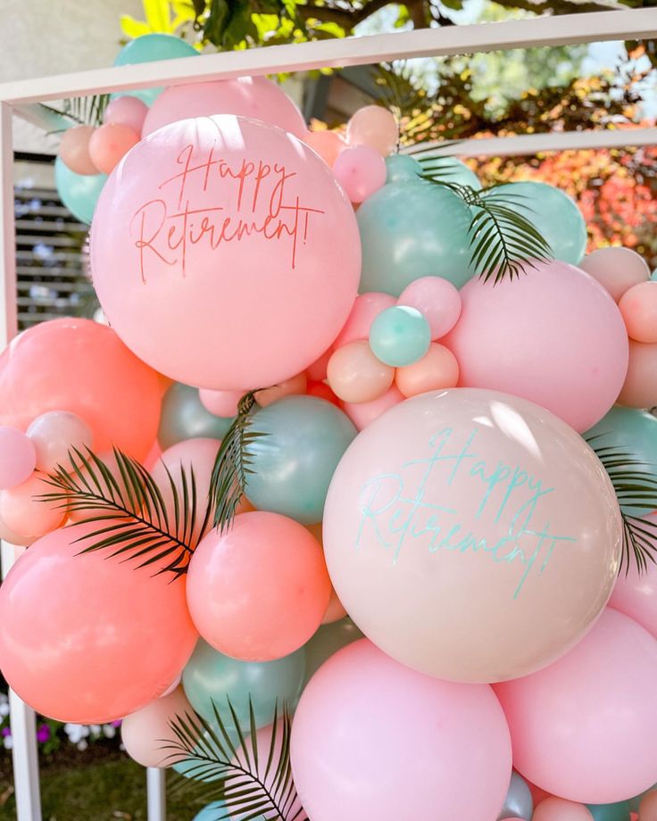 a bunch of balloons with happy birthday written on them in front of a frame and palm leaves