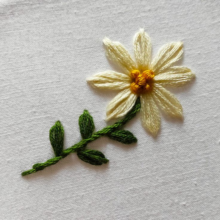 a close up of a flower on a piece of white fabric with green leaves and yellow center