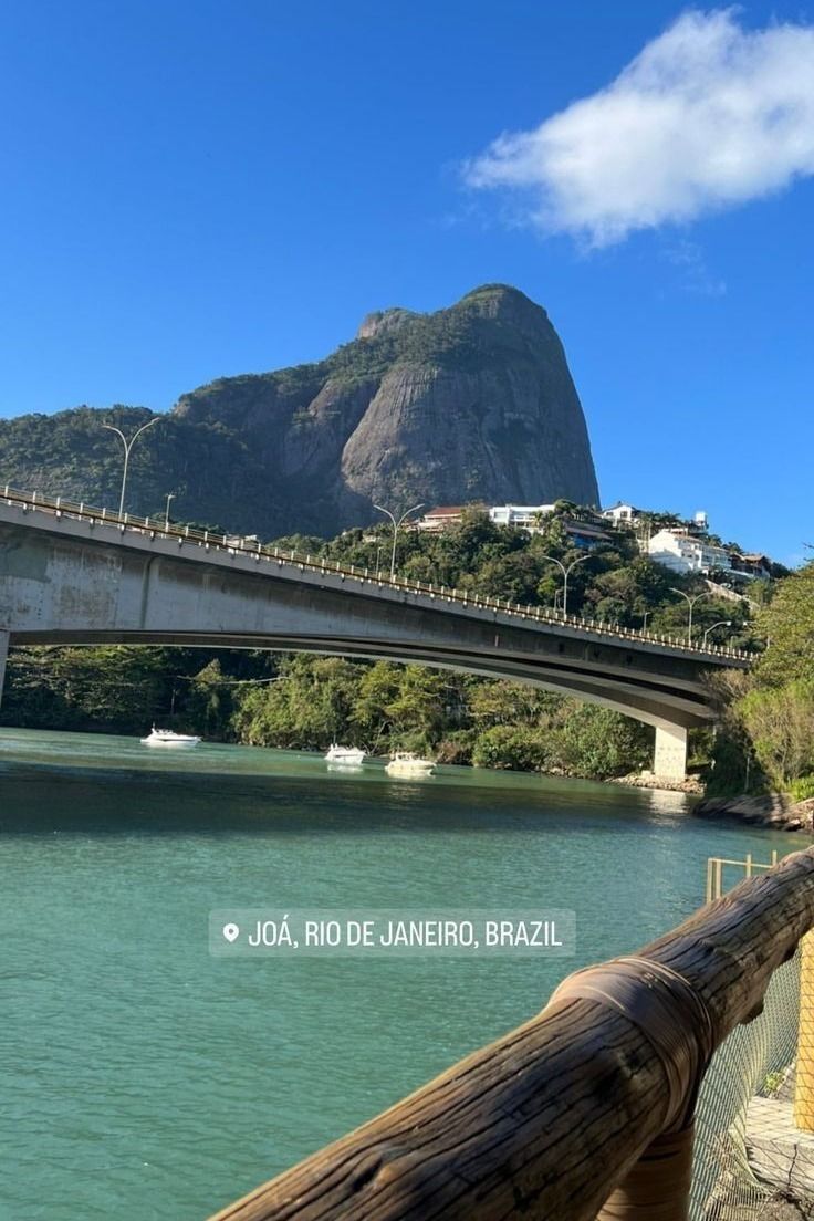 a bridge that is over some water with mountains in the backgroung and blue sky