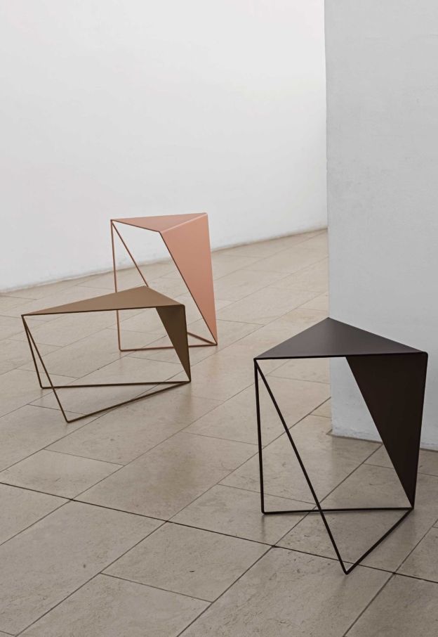 three different colored tables sitting on top of a tiled floor next to each other in front of a white wall