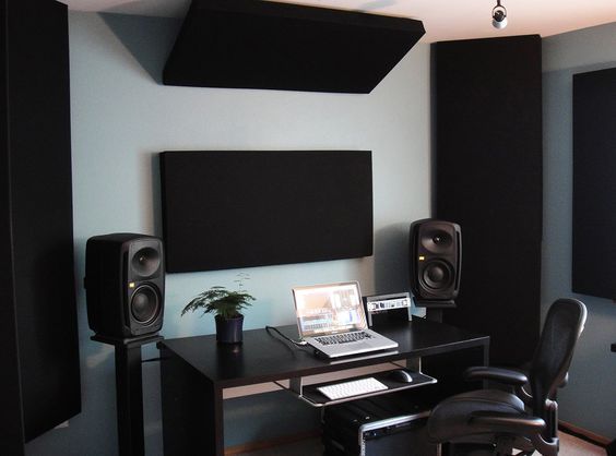 a computer desk with speakers and a laptop on it in front of a wall mounted speaker system