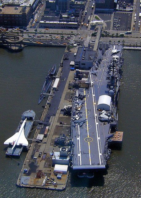 an aerial view of a navy ship docked in the water next to other boats and buildings