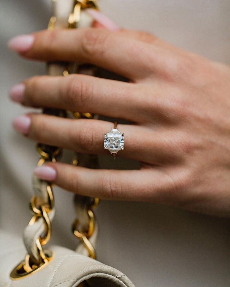 a woman's hand holding a gold chain with a diamond ring on it