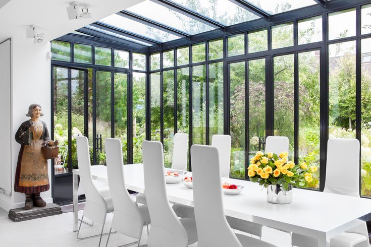 a dining room table with white chairs and a statue in the center surrounded by windows