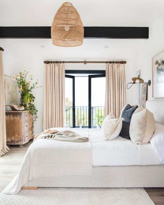 a bedroom with white bedding and beige drapes on the sliding glass doors leading to an outside patio