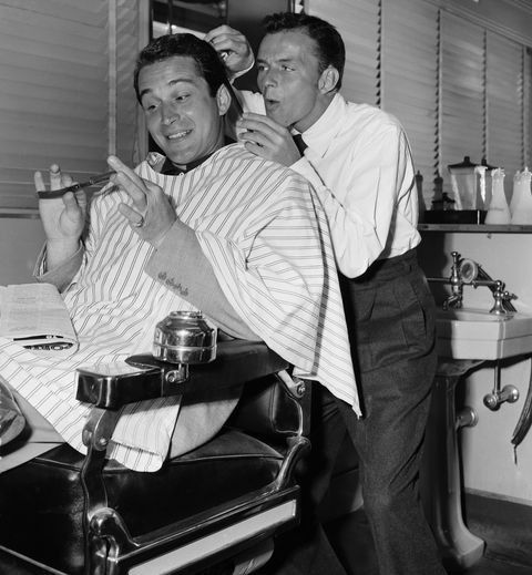 two men are brushing their hair in a barbershop and one man is sitting on the chair