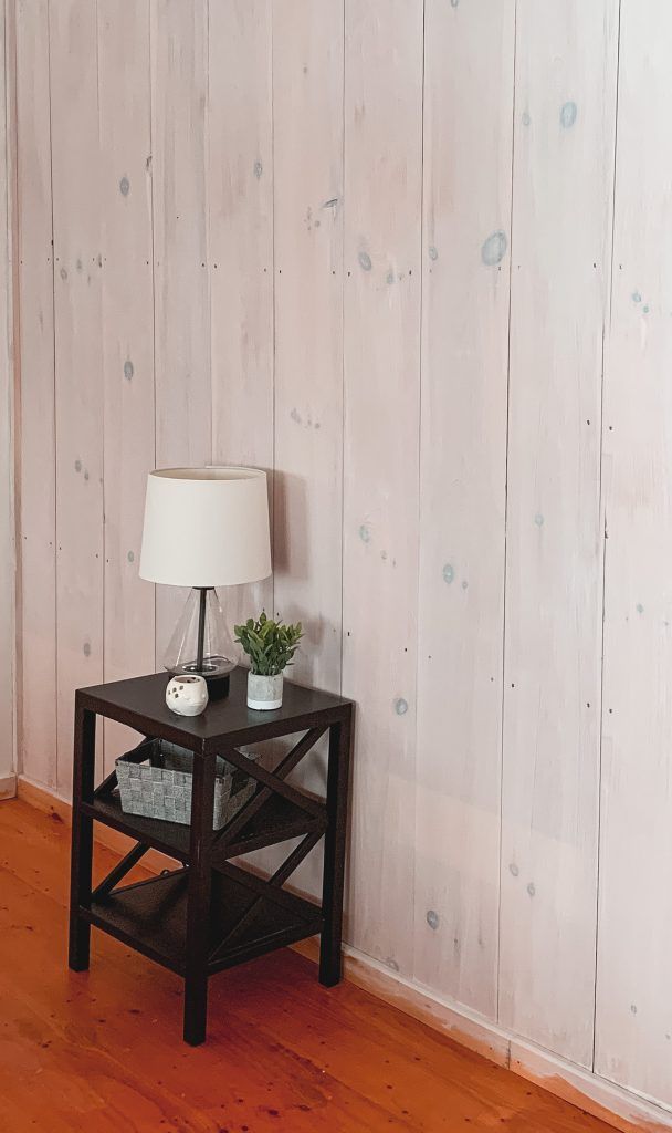 a small table with a lamp on it next to a wooden wall