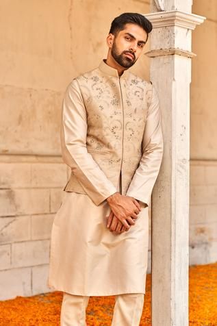 Beige bundi featuring floral motif zardozi embroidery. Paired with kurta and churidar.
Component: 3
Pattern: Embroidered
Type Of Work: Zardozi
Neckline: Mandarin Collar
Sleeve Type: Bundi: Sleeveless; Kurta: Straight Full
Fabric: Raw Silk, Chiniya Silk
Color: Beige
Other Details: 
Floral zardozi bundi
Pocketed bundi
Side slit kurta
Occasion: Groom - Aza Fashions Embroidered Waistcoat, Jayanti Reddy, Kurta Set For Men, Zardozi Embroidery, Nehru Jackets, Churidar, Kurta Set, Embroidered Silk, Couture Collection