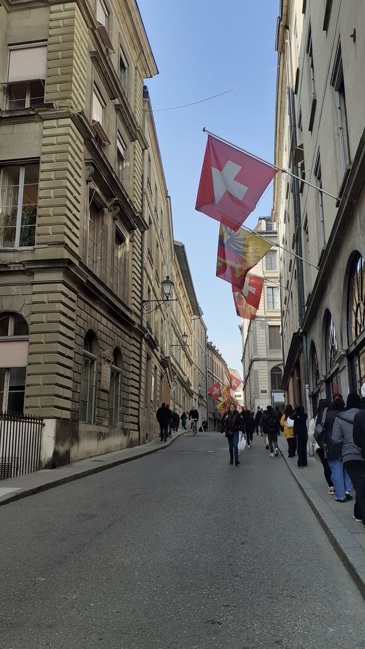 people walking down the street in an old european city with buildings and flags flying overhead