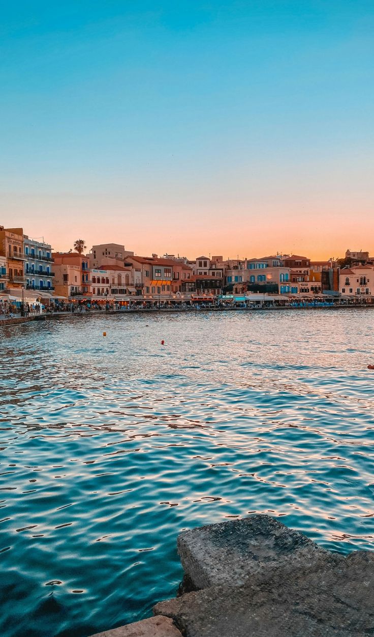 a body of water with buildings on the shore and people swimming in it at sunset