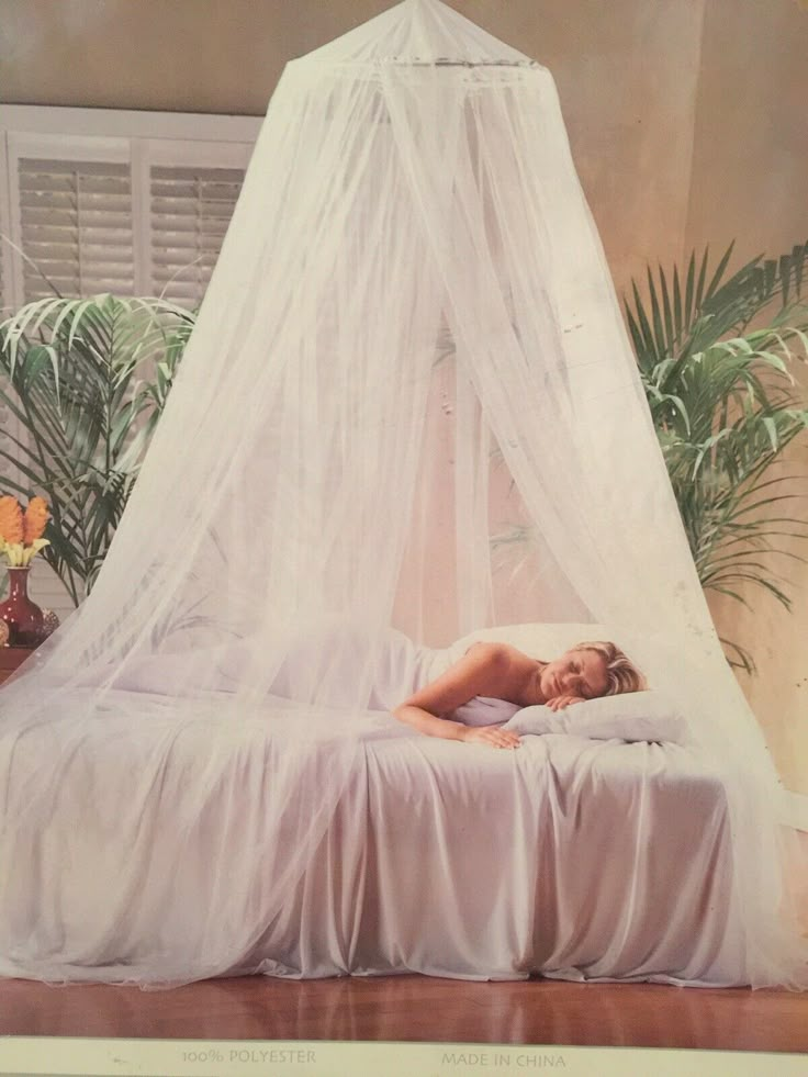 a woman is laying on a bed with a white canopy over it and plants in the background