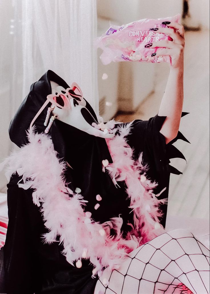 a woman wearing a mask and pink feathers on her head sitting on a bed with a pillow