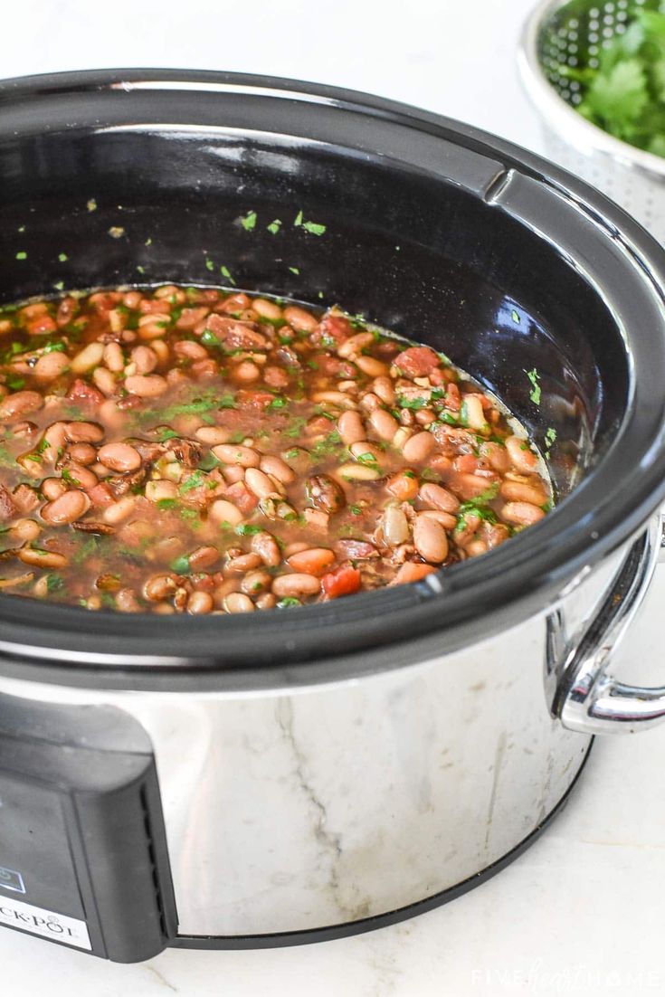 a slow cooker filled with beans and garnished with parsley on the side