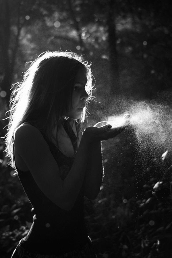 a woman standing in the woods spraying water on her hands with sunlight shining through trees behind her