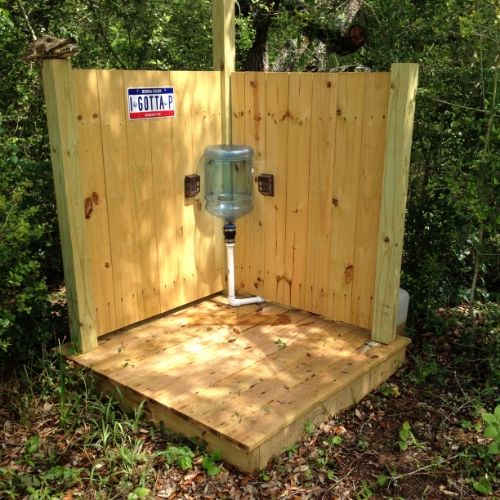 a wooden outhouse in the woods with a fan on it's back side