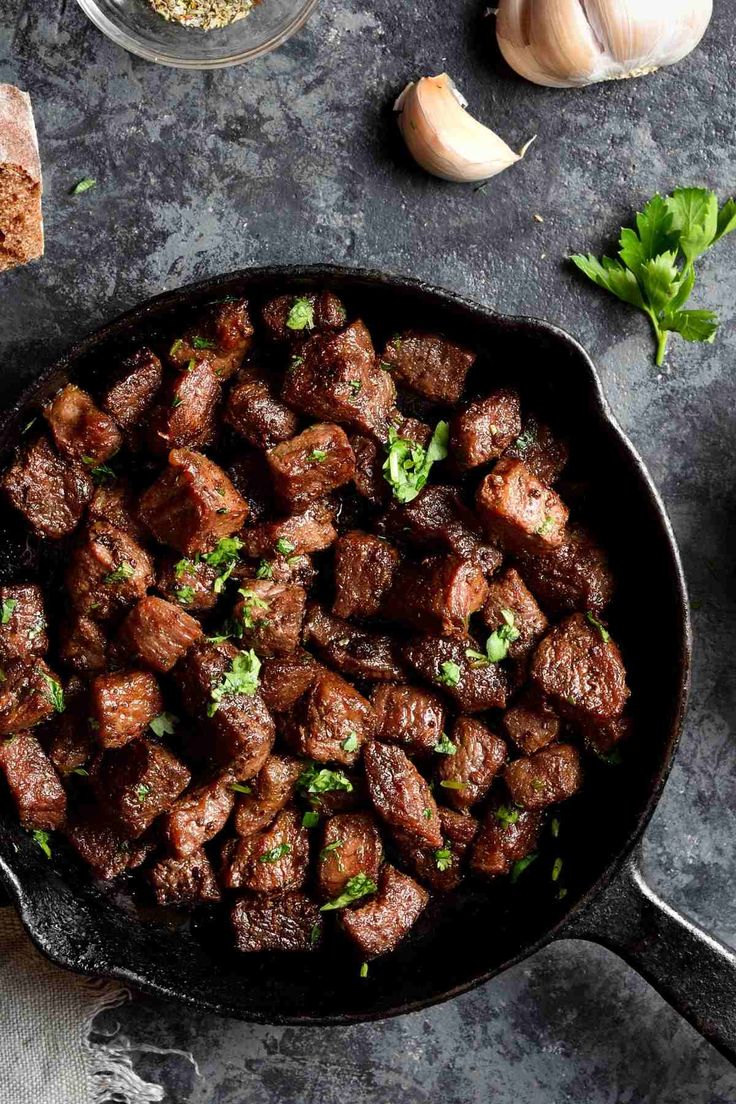 meat cubes in a skillet next to garlic, parsley and seasoning