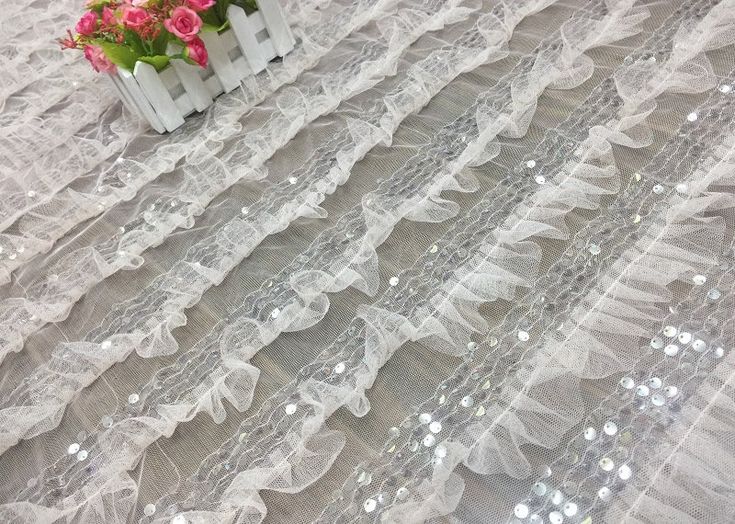 white sheer lace with sequins and flowers in vase on top of the table