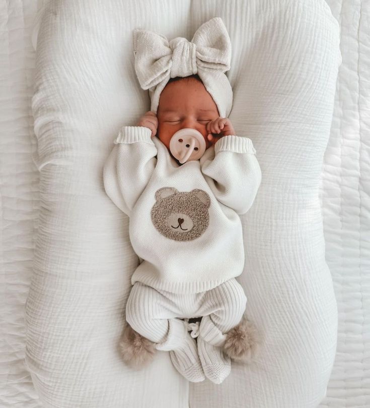 a baby is sleeping in a white outfit with a teddy bear on it's chest