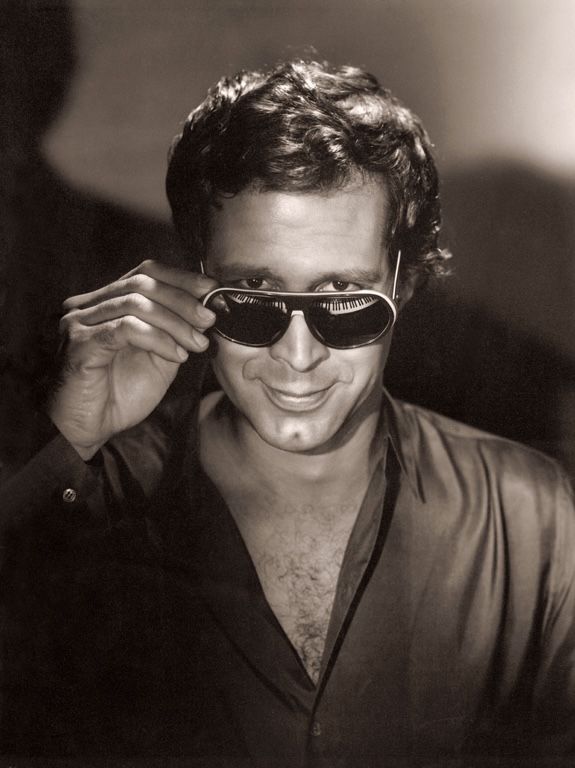 a man with sunglasses on his face and one hand to his ear, smiling at the camera