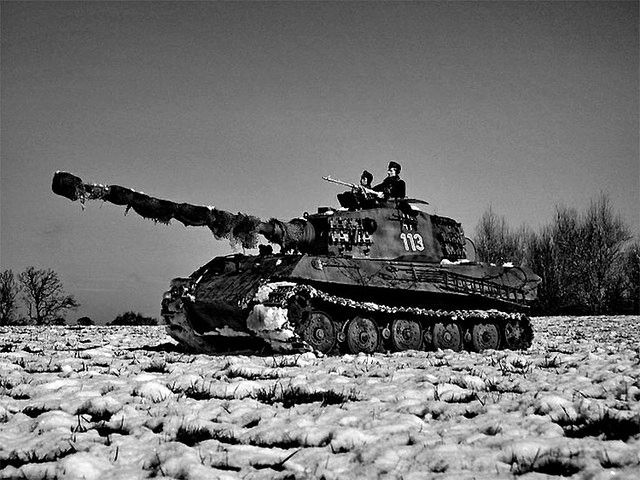 two men are sitting on top of a tank in the middle of a snowy field