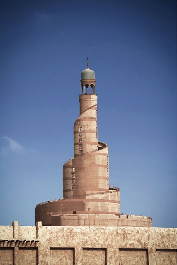 a tall tower with a clock on top of it next to a wall and blue sky