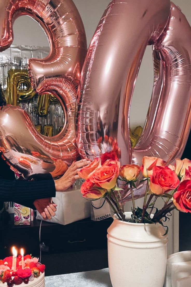 a woman is holding flowers and balloons in front of a table with two large numbers