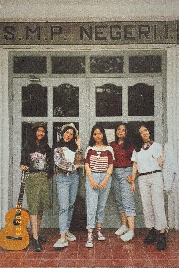 four young women standing in front of a door with an acoustic guitar on the floor