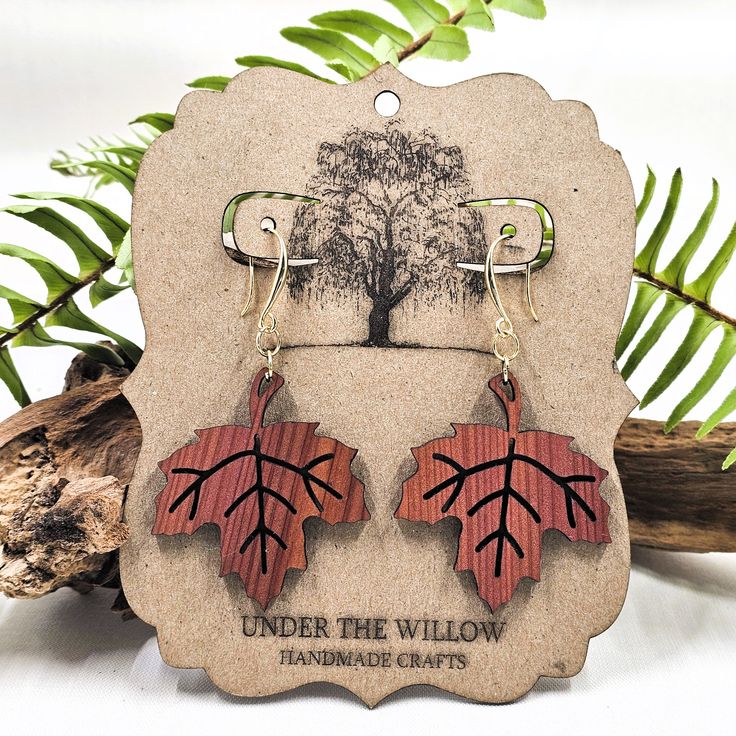 the earrings are made out of wood and have red leaves on them, with an oak tree in the background