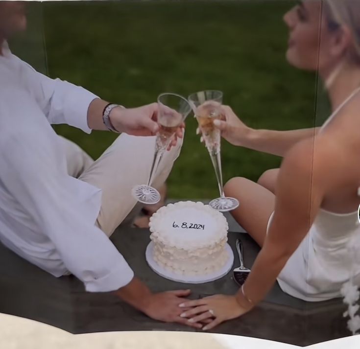 a man and woman sitting next to each other holding wine glasses in front of a cake