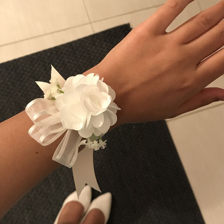 a woman's hand wearing a white flower wrist corsage