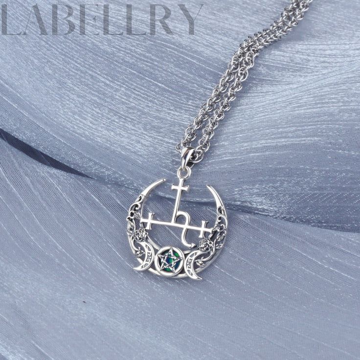 a silver necklace with an anchor and cross on the front, sitting on a blue fabric