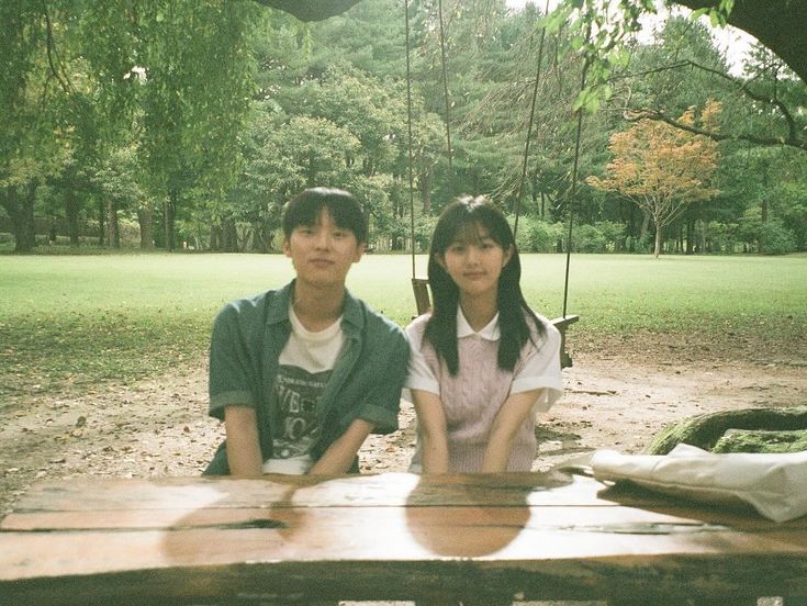 two people sitting on a wooden bench in a park